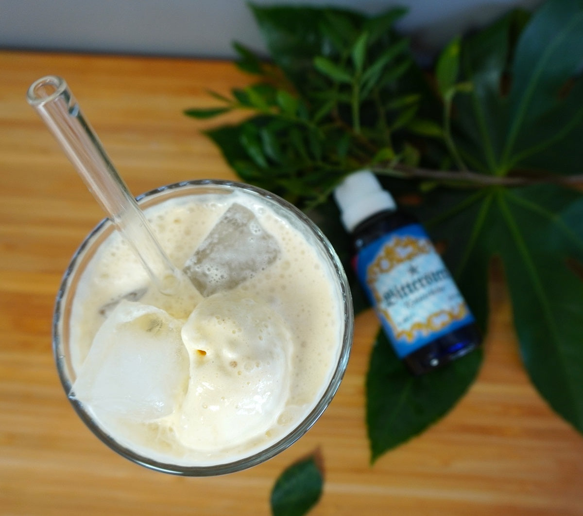 Erfrischender Eiskaffee mit Eiswürfeln und Vanilleeis in einem Glas, daneben eine Flasche Bitterstern Tropfen auf einem Holzuntergrund mit grünen Blättern – Rezeptidee für einen sommerlichen Bitterkaffee-Drink.