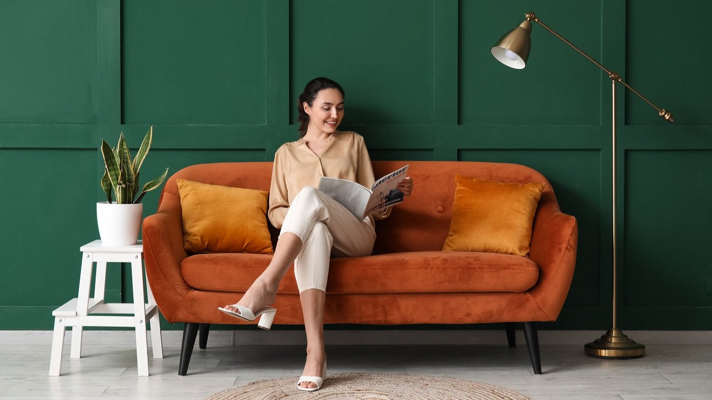 Frau liest ein Magazin auf einem orangenen Sofa vor einer grünen Wand