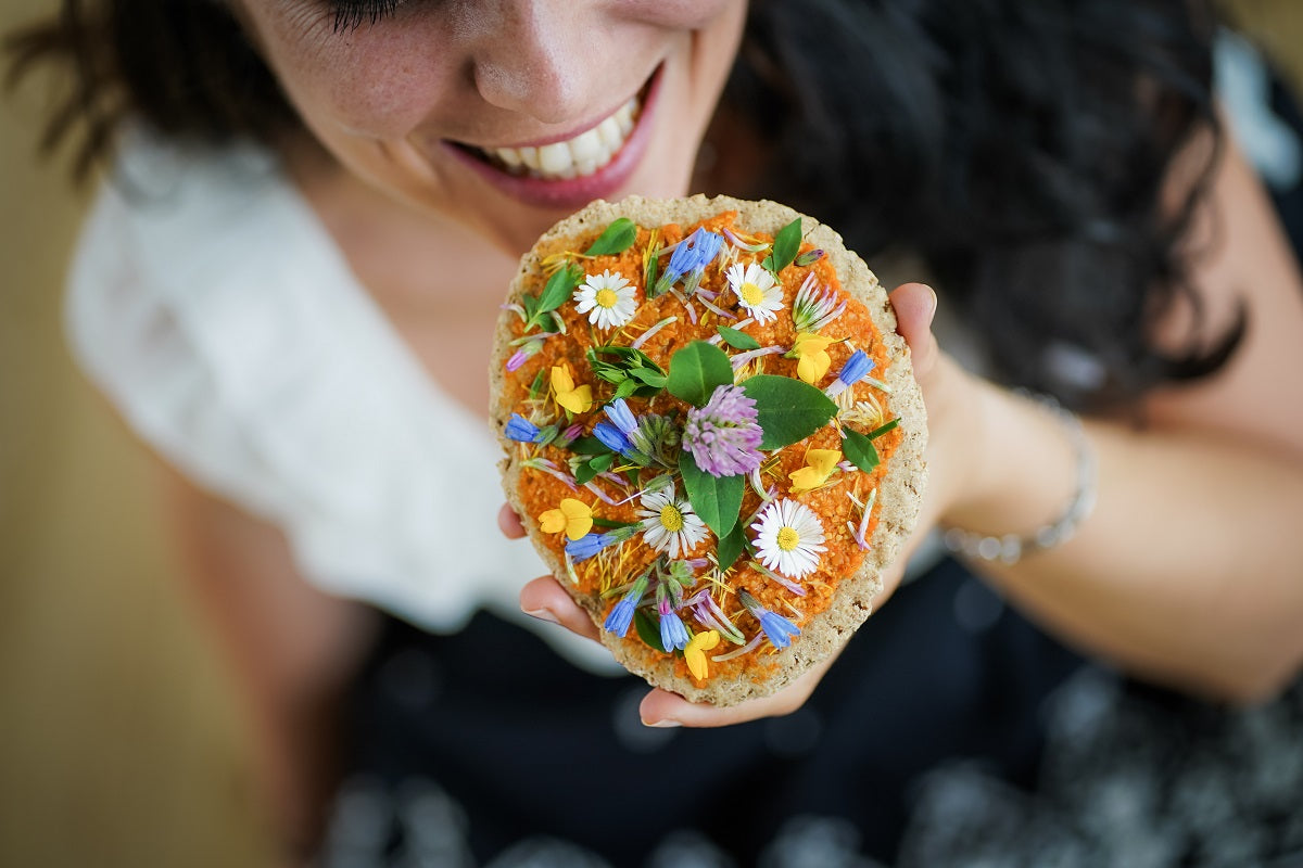 Frau beißt in ein Brot mit Kräutern und Gänseblümchen