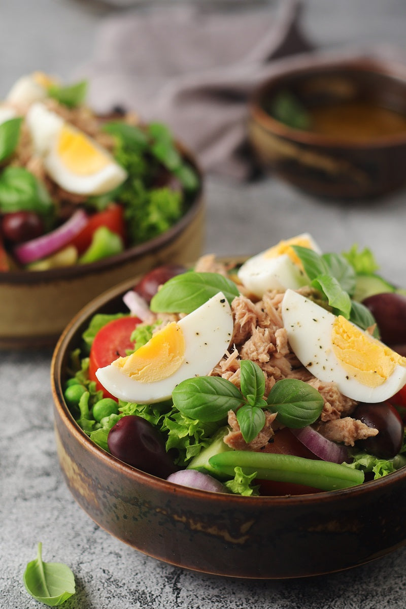 Nicoise Salat angerichtet in braunen Schalen auf einem hellen Steintisch