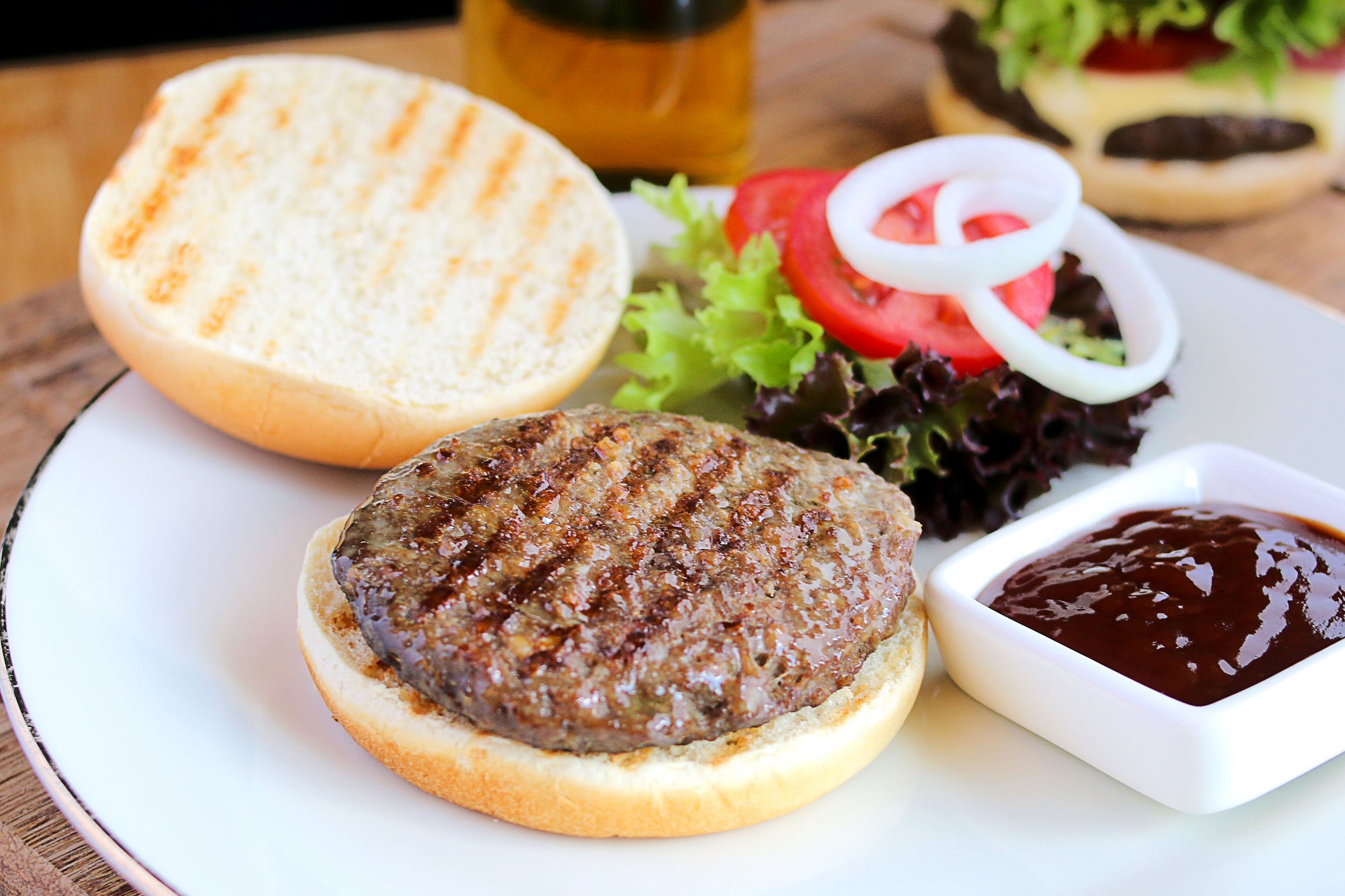 Burger mit Zwiebeln, Salat und Soße auf einem weißen Teller