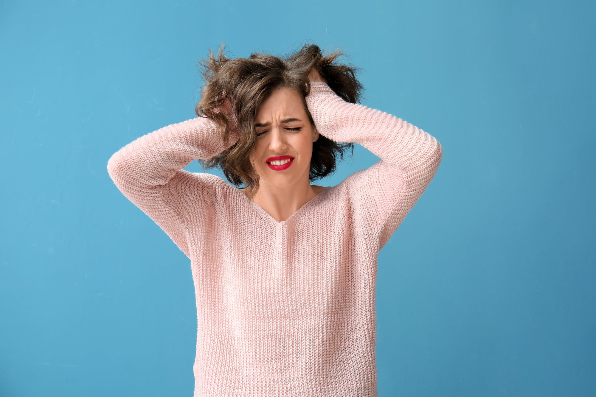 Junge Frau mit verzweifeltem Gesichtsausdruck greift sich frustriert mit beiden Händen in die Haare – Symbolbild für Unzufriedenheit.