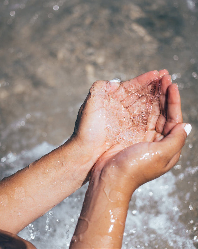 Wasser in den zu einer Schüssel geformten Händen einer Person aus einer Quelle zum Trinken.