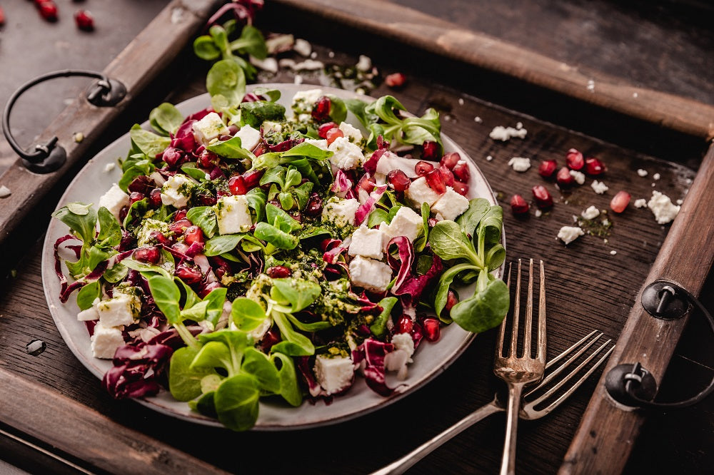 Bittere Lebensmittel wie, Feldsalat, Radicchio und Granatapfel als Salat auf einem Teller angerichtet.