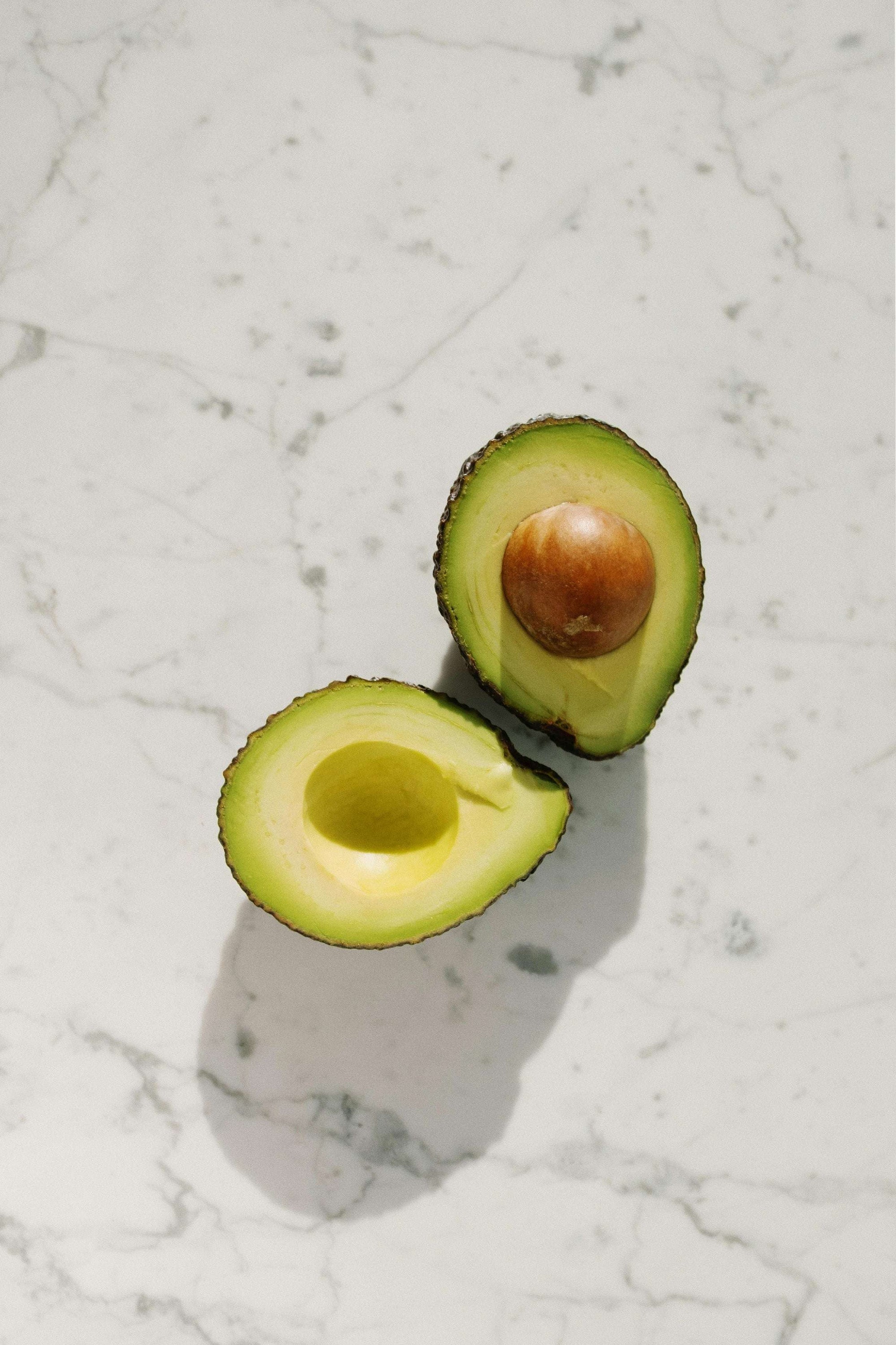 In zwei Hälften aufgeschnittene. frische Avocado auf einer weißen Marmorplatte