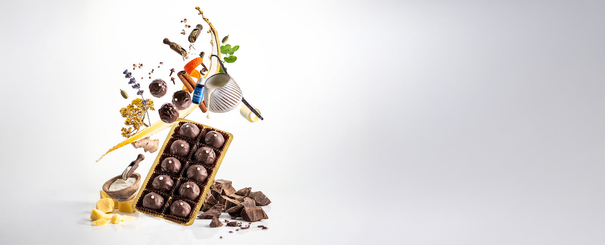 Bittertstern Schokoladentrüffel mit all seinen Zutaten, von Lavendel, Zimt, Ingwer bis Kakao - schwebend dargestellt, sowie 3 fliegenden Pralinen über dem Produkt