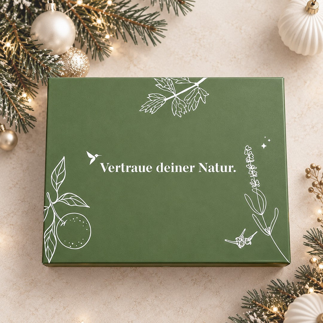 Geschlossener Bitterstern Trüffel Adventskalender in grüner Geschenkbox mit der Aufschrift ‚Vertraue deiner Natur‘, weihnachtlich dekoriert mit Tannenzweigen, Kugeln und Lichtern.