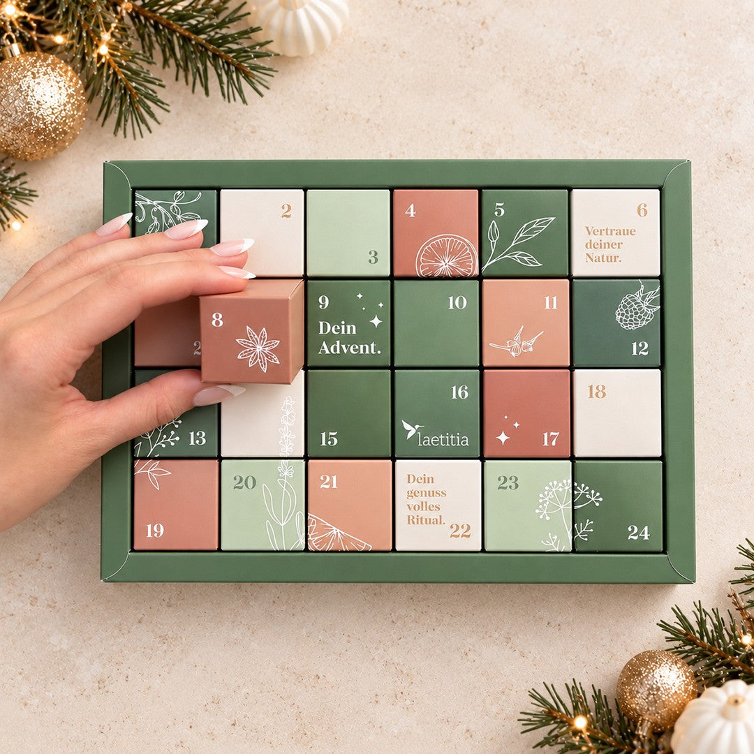 Geöffneter Bitterstern Trüffel Adventskalender mit 24 nummerierten Schachteln, eine Hand entnimmt das Türchen Nummer 8.