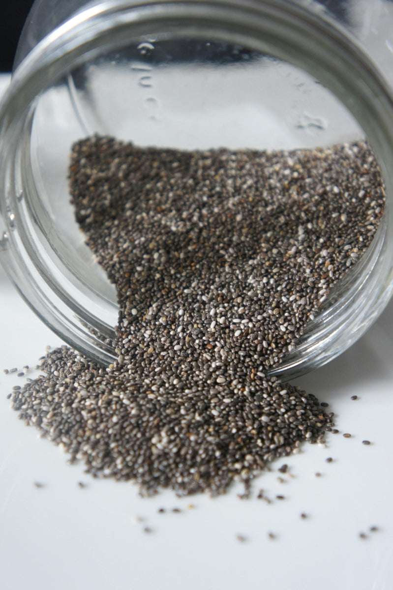 Chia Samen fließen aus einem umgekippten Glas auf eine weiße Oberfläche