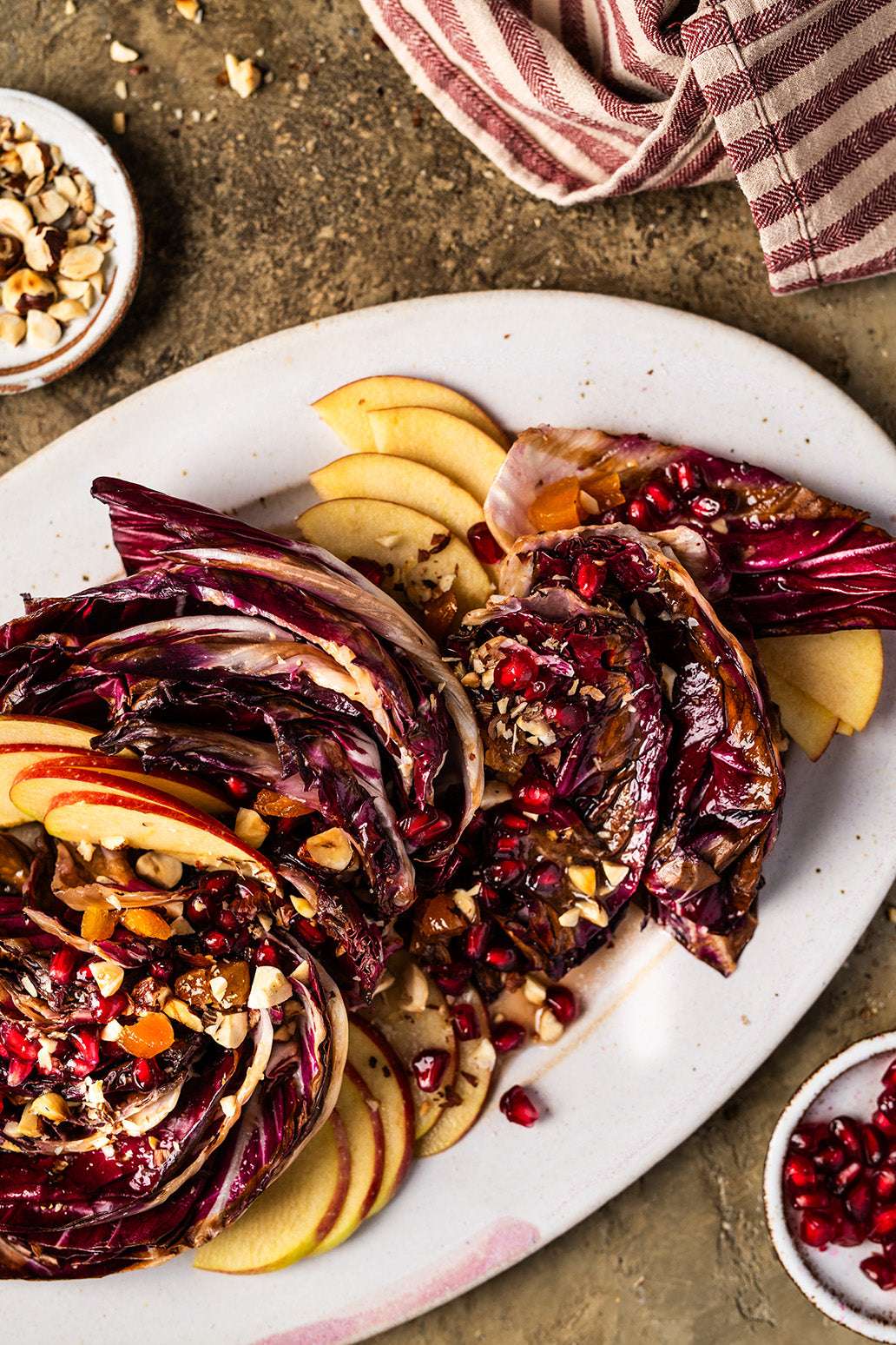 Gegrillter Radicchio mit dünnen Apfelscheiben und Granatapfel auf länglichem Teller
