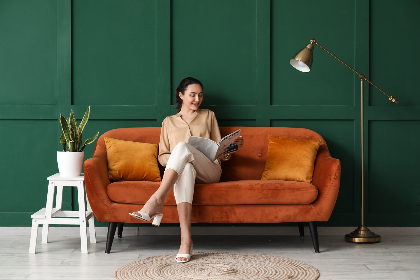 Frau liest ein Magazin auf einem orangenen Sofa vor einer grünen Wand