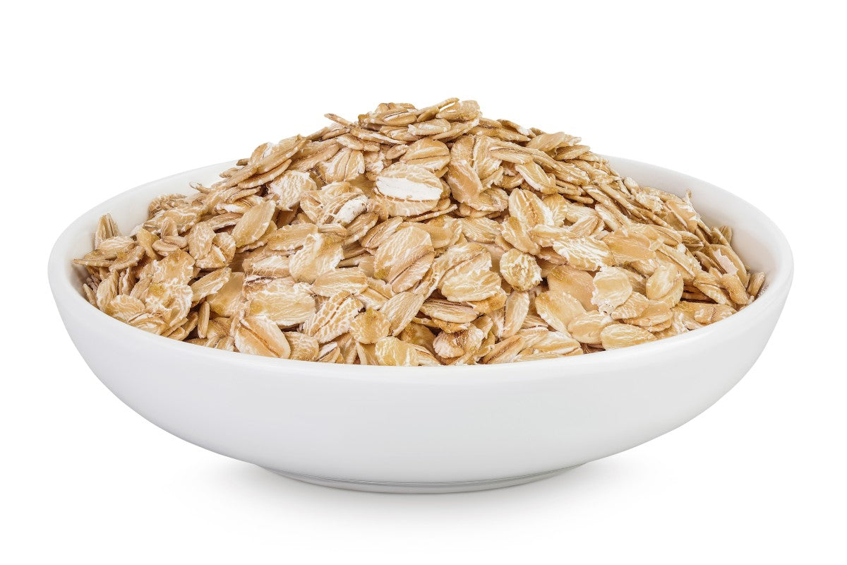 Eine weiße Schüssel, gefüllt mit Haferflocken, vor hellem Hintergrund. Die Flocken sind grob und naturbelassen und dienen als Basis für Hafermilch.