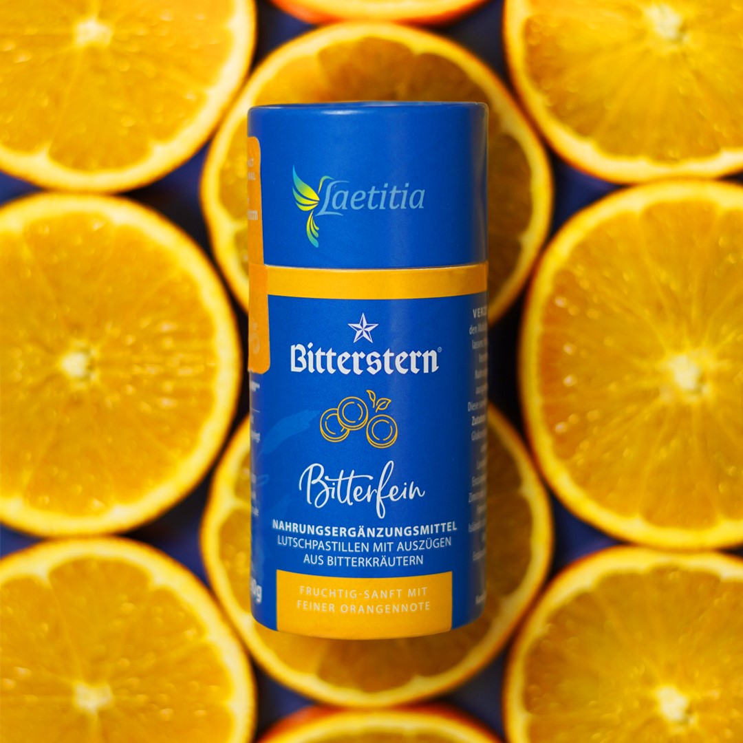 Dose Bitterstern Bitterfein Lutschpastillen von Laetitia vor Hintergrund aus aufgeschnittenen Orangenhälften, Produktetikett in Blau und Orange.