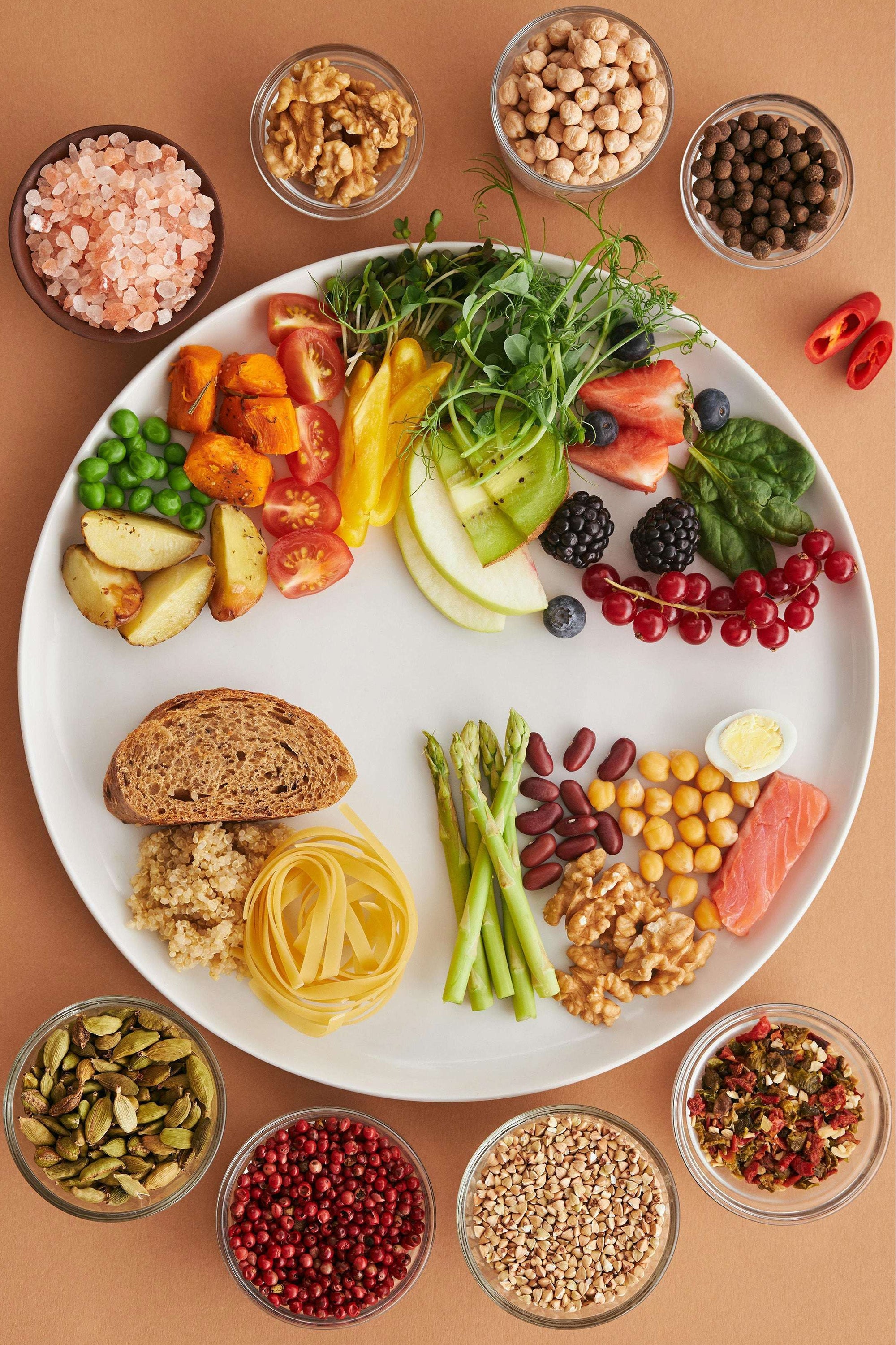 Mehrere kleine Schälchen auf hellem Untergrund um einen Teller gefüllt mit unterschiedlichen ballaststoffreichen Lebensmitteln: Die Schalen sind harmonisch arrangiert und vermitteln eine gesunde, pflanzlich betonte Ernährung mit Fokus auf Ballaststoff