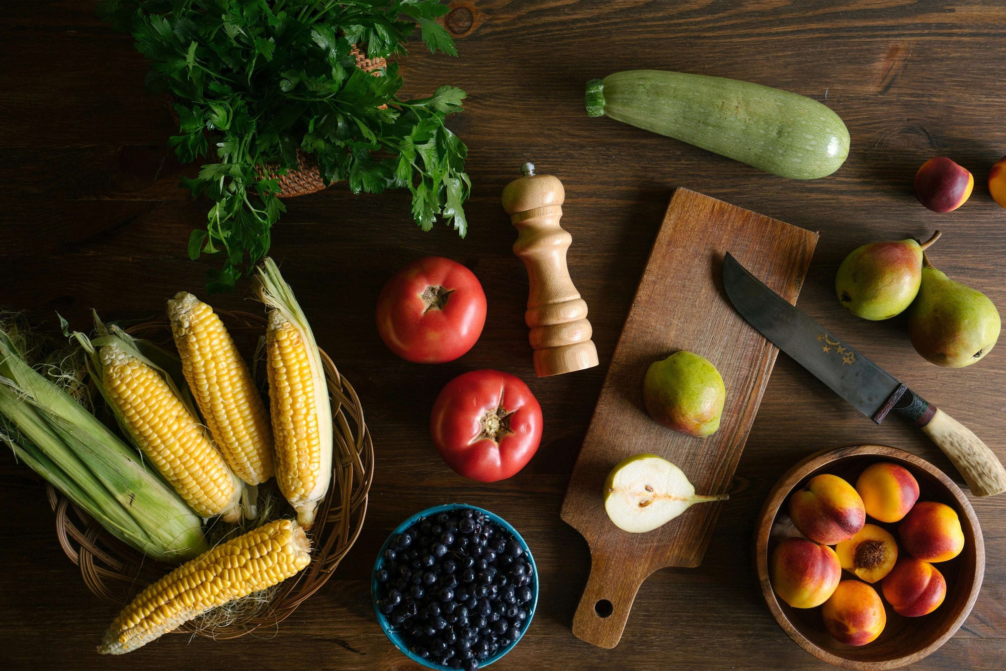 Arrangement aus frischem Obst ballaststoffreichem Gemüse: Zu sehen sind Tomaten, Maiskolben, grüne Zucchini, Petersilie, Birnen und Nektarinen. in der Mitte ist ein Schneidebrett mit einem Messer und einer halbierten Birne. Die Farben wirken lebendig und die Zutaten vermitteln eine gesunde, pflanzlich-reiche Ernährung.