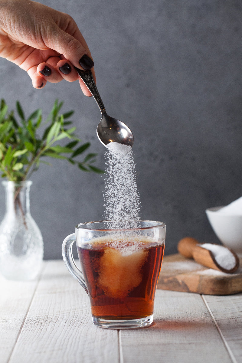 Stevia wird von einem Teelöffel in eine Tasse Tee geschüttet. 