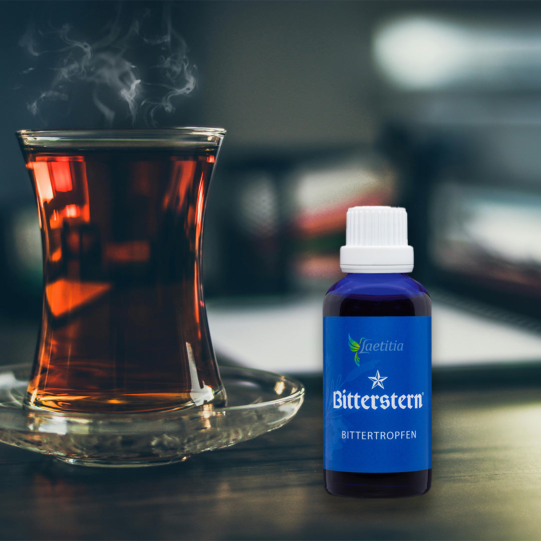 Noch dampfender aufgebrühter Schwarztee mit einer Flasche Bitterstern Bittertropfen im Vordergrund