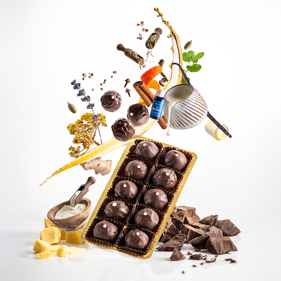 Bitterstern Schokoladentrüffel mit all seinen Zutaten, wie Kakao, Milchpulver, aber auch Lavendel, Zimtrinde, Ingwer, usw. schwebend dargestellt