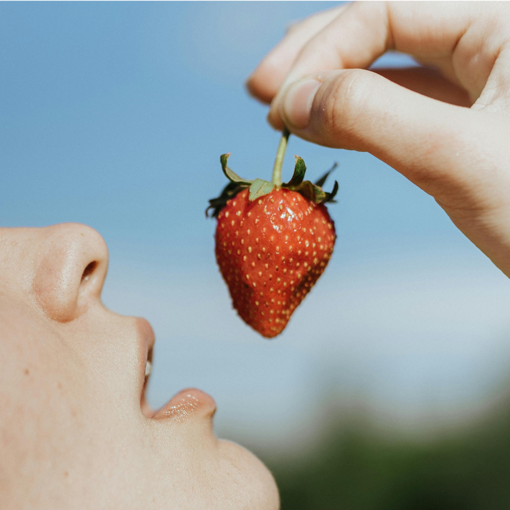 Jemand hält eine Erdbeere über den geöffneten Mund