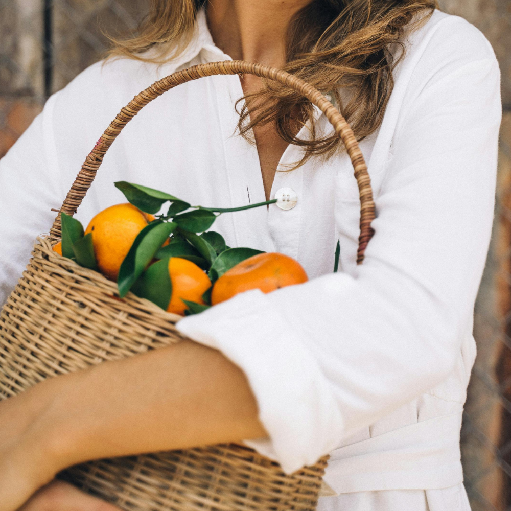 Frau mit langen Haaren trägt einen Korb mit frisch gepflückten Mandarinen