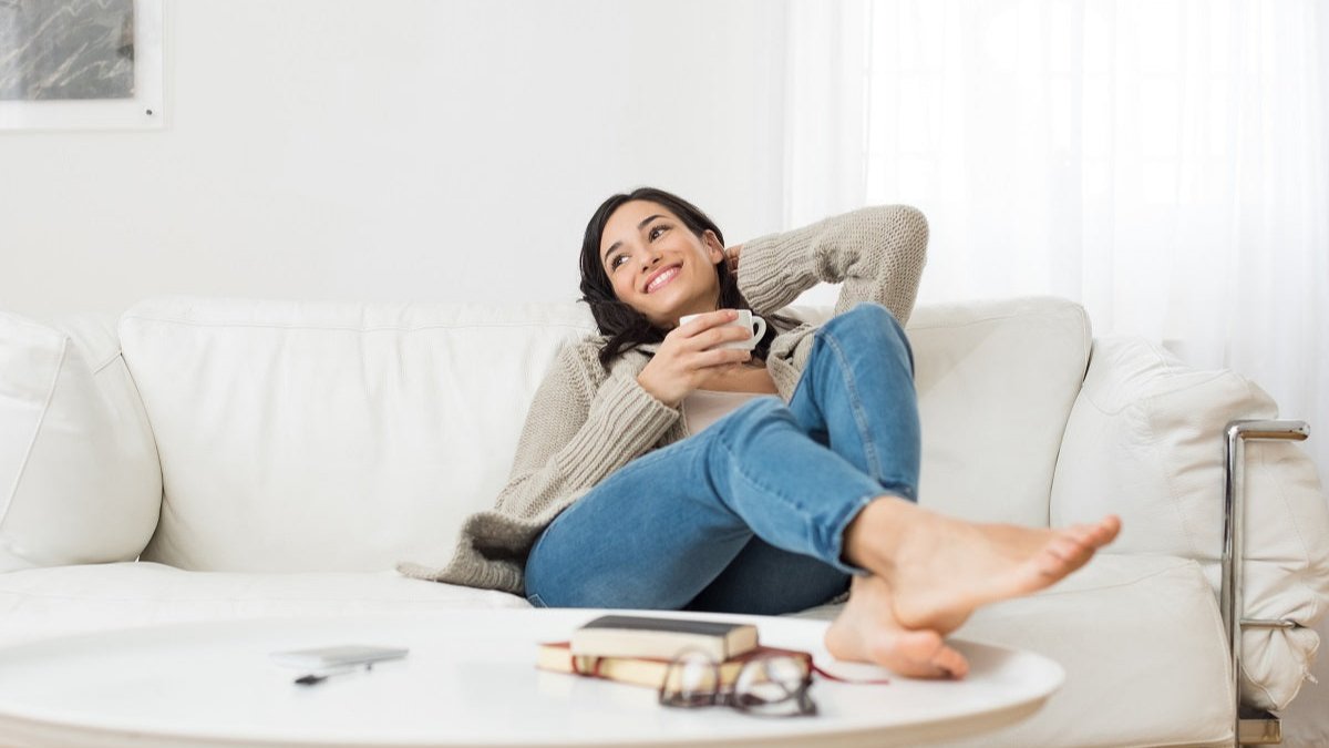 Frau sitzend auf einem Sofa mit einer Tasse Tee beim Stress abbauen