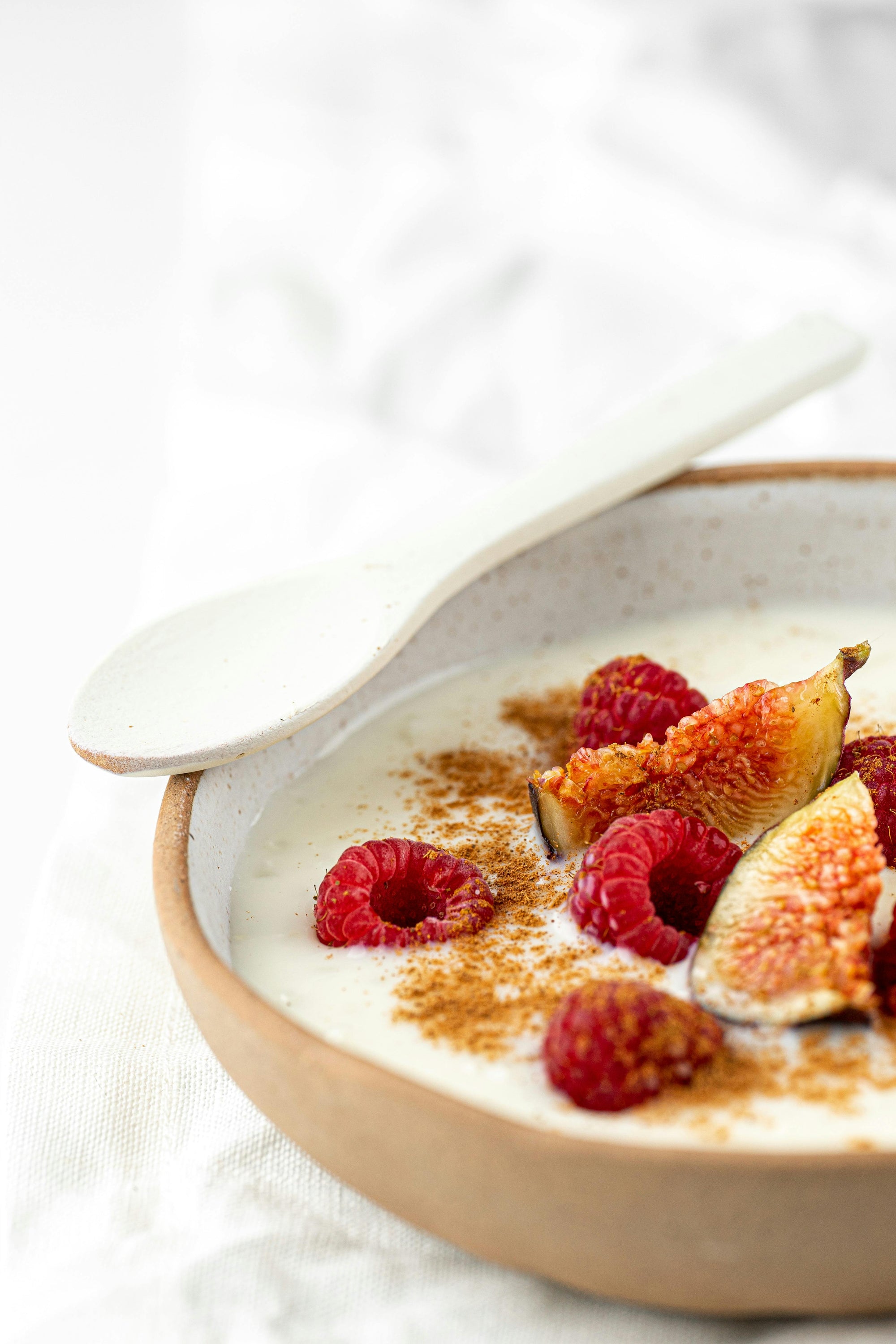 Naturjoghurt mit Himbeeren, Feigen und Zimt in einer Keramikschale. Das Bild steht im Zusammenhang mit der Frage, ob Joghurt basisch oder säurebildend wirkt.