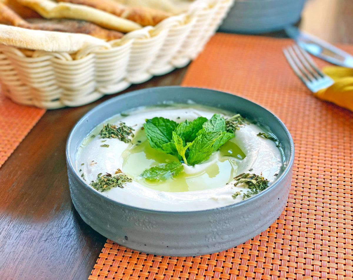 Schale mit cremigem Joghurt, frischer Minze, Olivenöl und Kräutern auf einem gedeckten Tisch. Das Bild begleitet einen Beitrag zur Frage, ob Joghurt basisch ist und wie er im Säure-Basen-Haushalt eingeordnet wird.