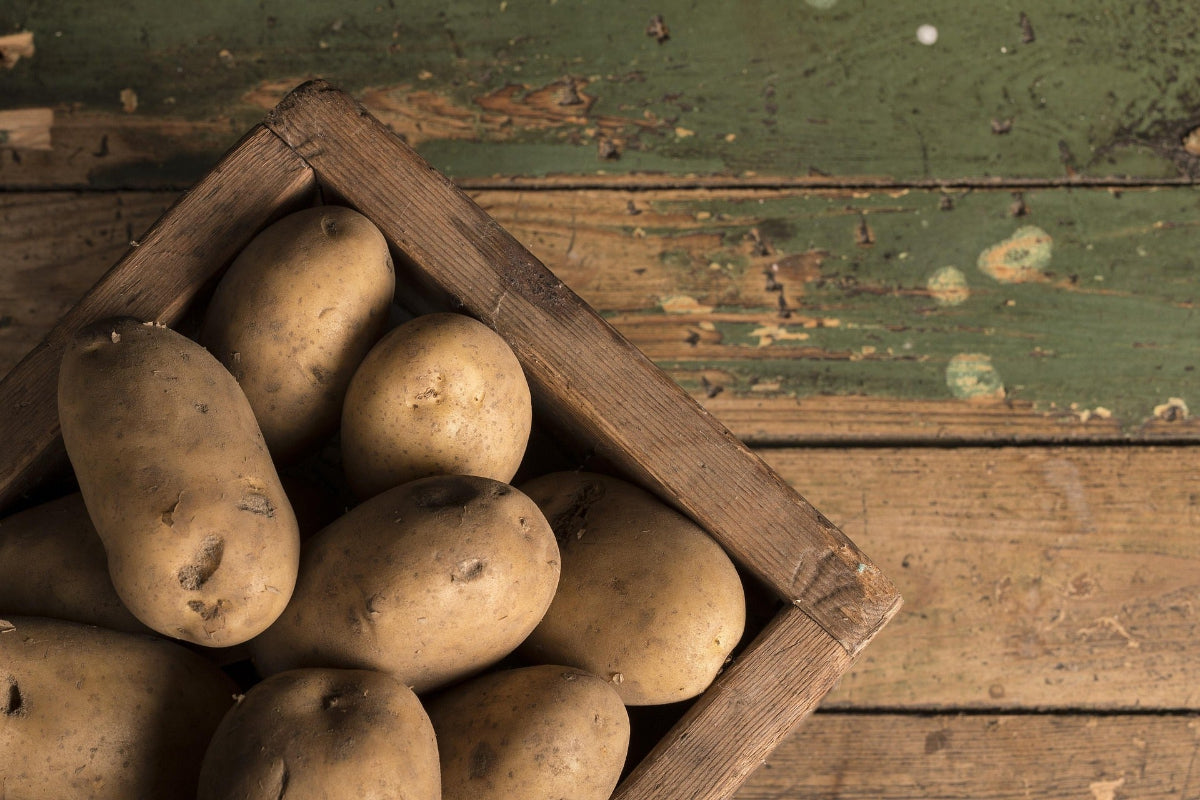 Rohe Kartoffeln in einer Holzkiste auf rustikalem Holztisch – Symbolbild zur Frage, ob Kartoffeln basisch oder säurebildend sind und wie sie in die basische Ernährung passen.