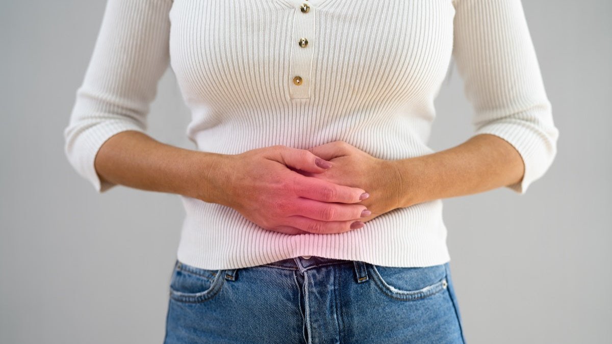 Frau mit weißem Pullover hält sich den Bauch wegen Reizdarm.