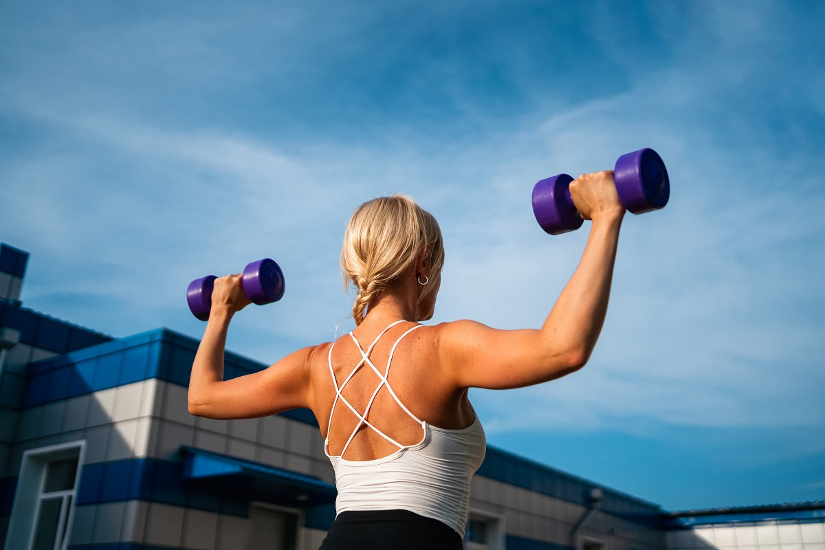 Blonde Frau macht Krafttraining mit Hanteln im Freien