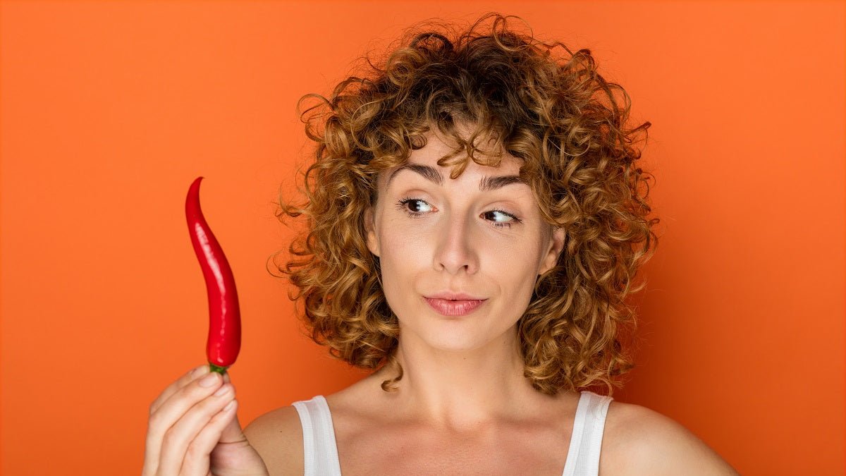 Frau mit Chili in der Hand vor orangenem Hintergrund. Scharfes, wie Chili verusacht oft Sodbrennen