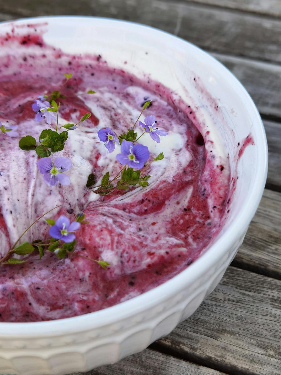 Cremiger Skyr mit Beerenpüree in einer weißen Schale, dekoriert mit essbaren lila Blüten. Das proteinreiche Milchprodukt steht im Zusammenhang mit der Frage, ob Skyr basisch oder säurebildend wirkt.