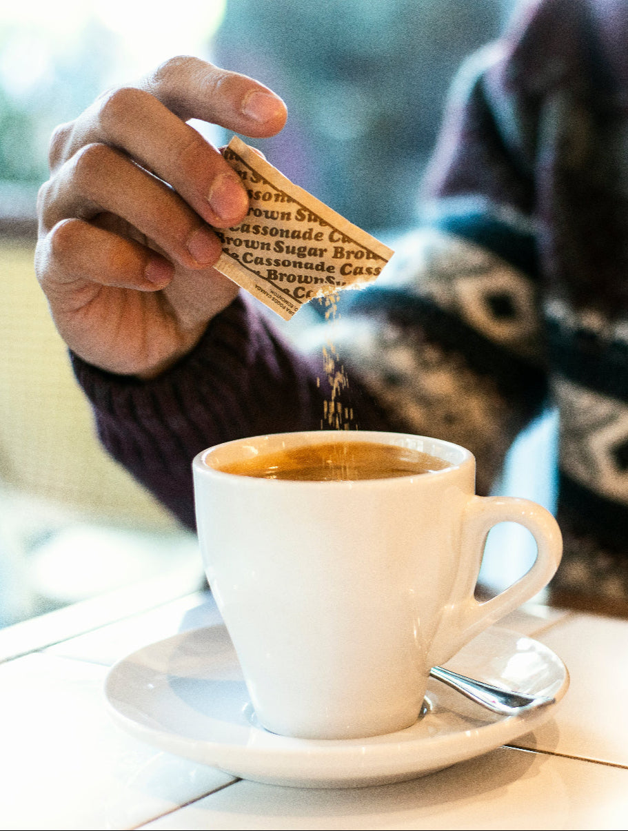 Mann gibt Süßstoff aus einem Tütchen in seinen Kaffee