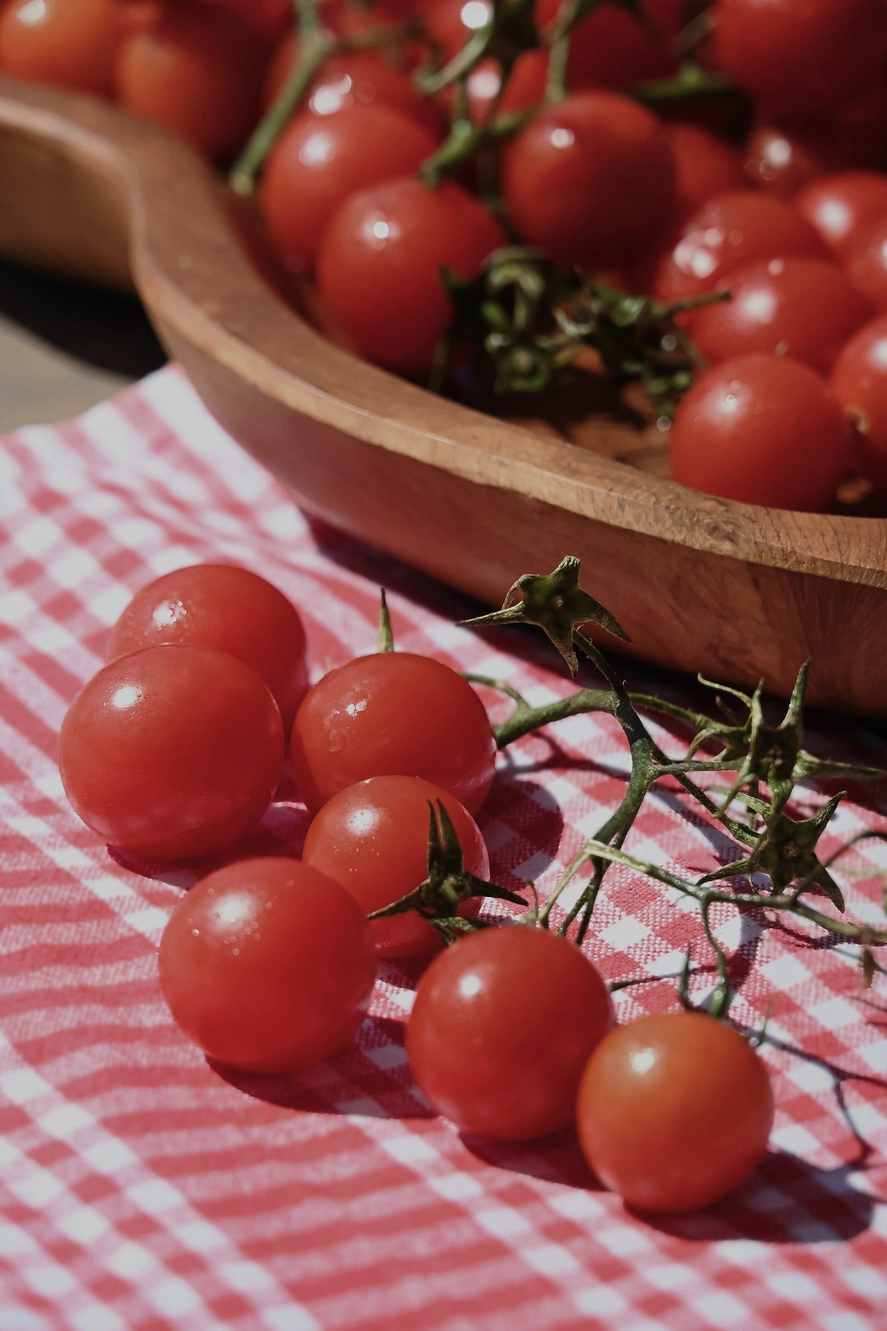 Frische Cherrytomaten liegen auf einem rot-weiß karierten Tuch neben einer Holzschale mit weiteren Tomaten – Symbolbild zur Frage, ob Tomaten basisch oder säurebildend sind.