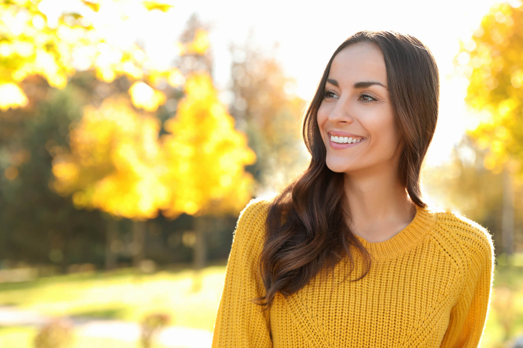 Eine lächelnde Frau mit gelbem Pullover in der herbstlichen Natur 