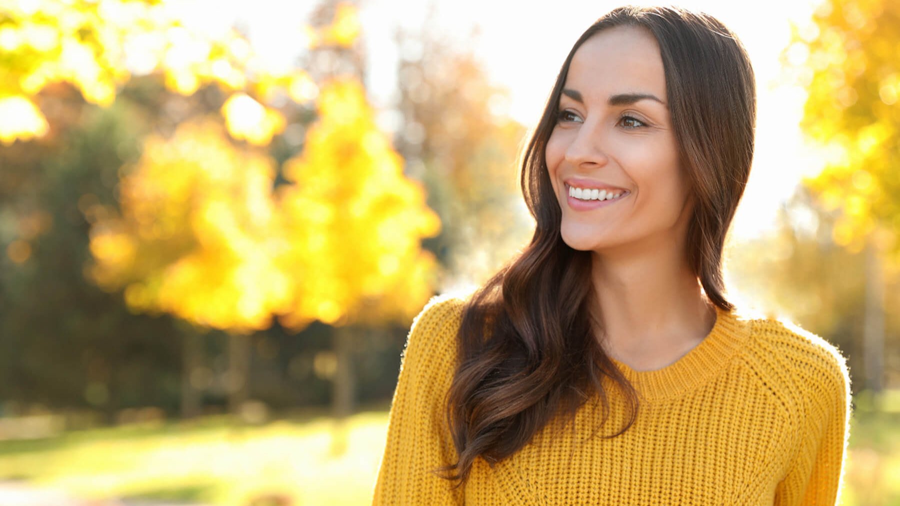 Eine lächelnde Frau mit gelbem Pullover in der herbstlichen Natur 